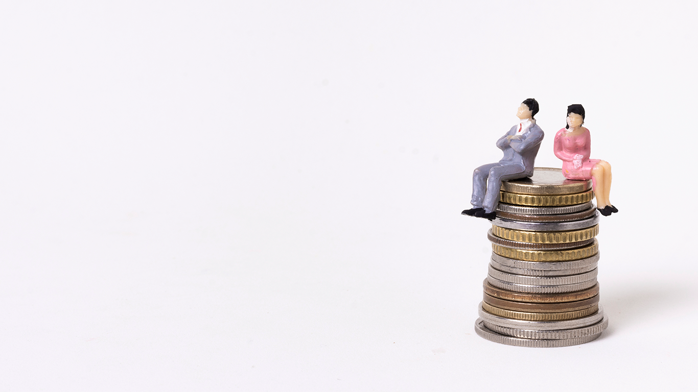 Figurines of a business man and woman sitting on top of coins to represent their businesses' cost savings
